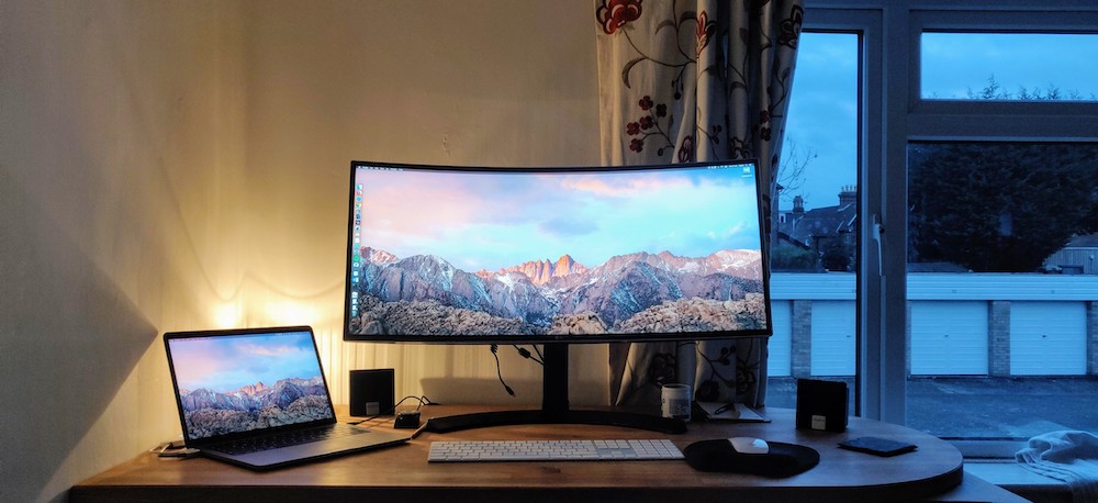 Laptop screen and widescreen monitor inside lamp lit room