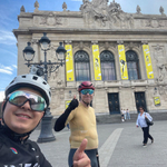 Calum and Luis in cycling wear outside Lille's City Hall draped in Tour de France banners