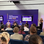 Panel on “Living with Imposter Syndrome” at TechShare Pro 2025, with 5 speakers, a sign language interpreter, and audience watching. Microsoft sponsorship visible.
