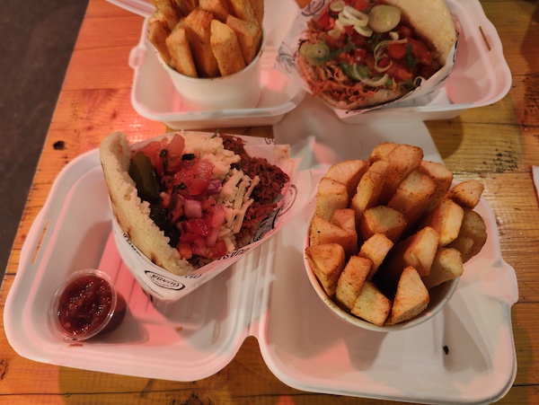 Two arepas with Yuca frita and spicy sauce in a takeway box