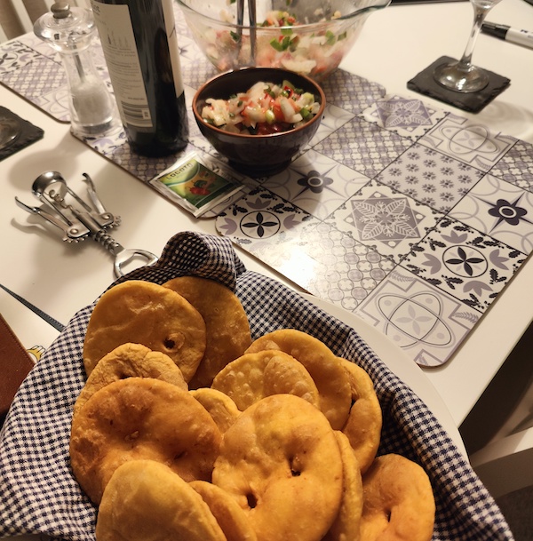 a large plate of sopaipas on a tea-towel, wine bottle and bowl of pebre