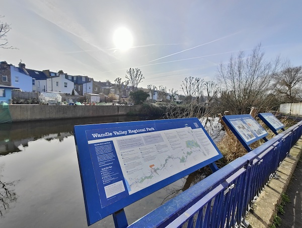 River Wandle with interpretation boards and trees in background