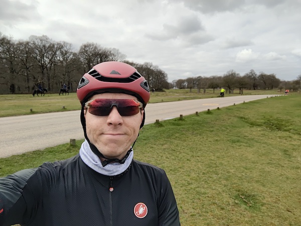 Calum in red sunglasses and cycling helmet with backdrop of Richmond Park