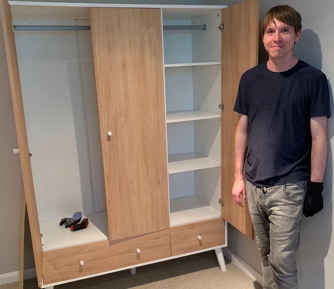 Calum beside a part assembled 3-door wardrobe