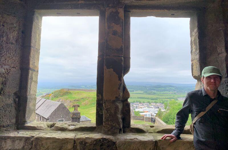 Calum with backdrop of unglazed castle window looking over Central Scotland hills.