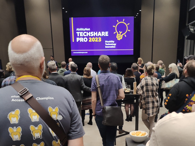 people standing in front of presentation screen with the text, TechShare Pro 2023, on a purple background