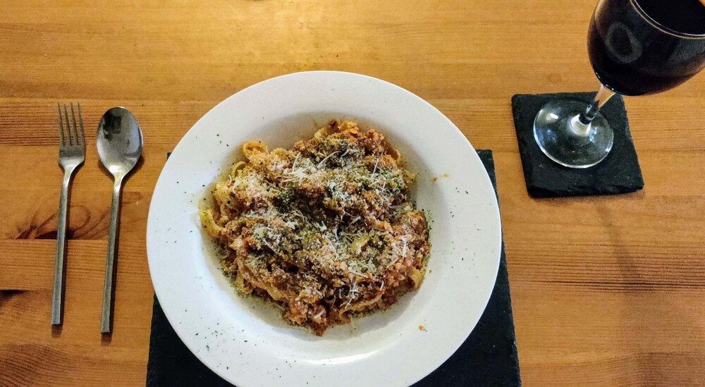 Tagliatelle cauliflower lentil bolognese in circular plate with wine on a wooden table