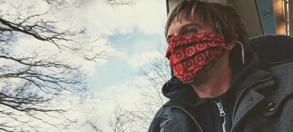 Calum on a train wearing London Eye decorated red face mask