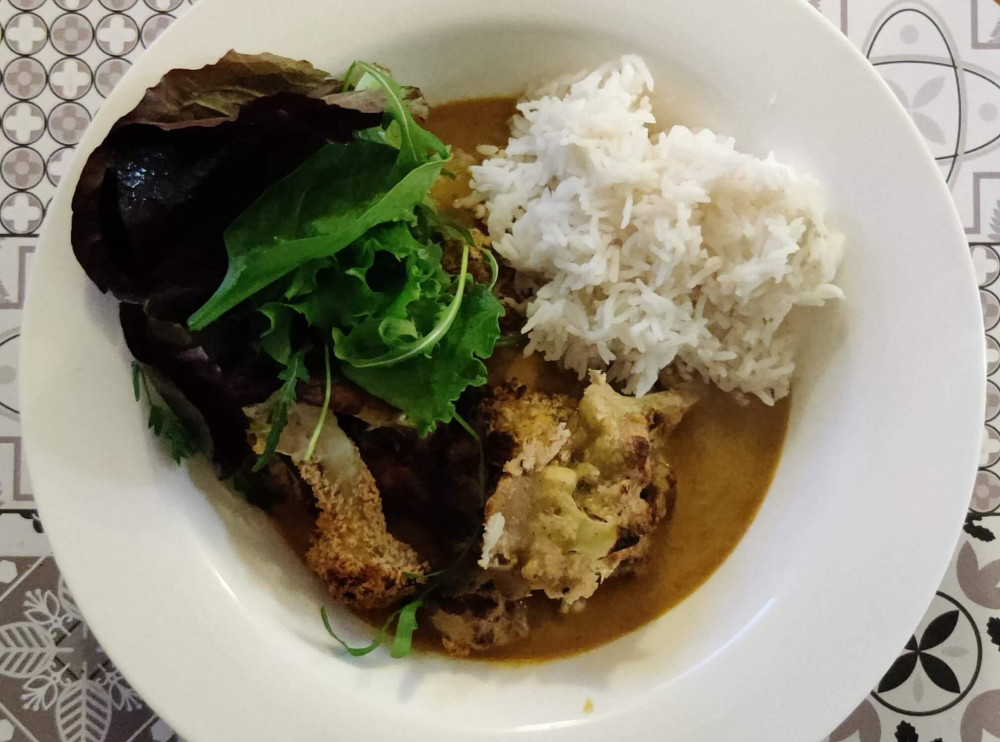 Katsu curry with cauliflower, greens and white rice in a white bowl