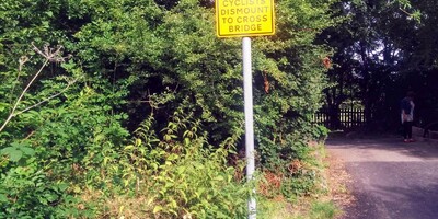 Yellow signpost - cyclists dismount to cross bridge on roadside