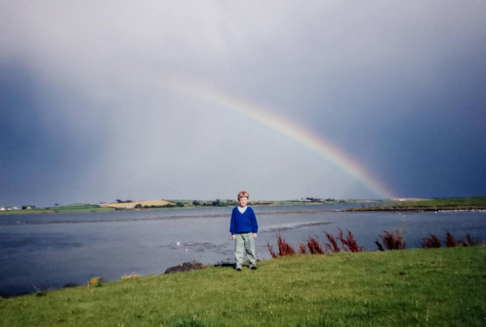 Calum beside the Lecale Peninsular with half a rainbow in the backdrop