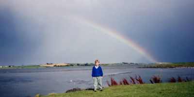 Calum beside the Lecale Peninsular with half a rainbow in the backdrop