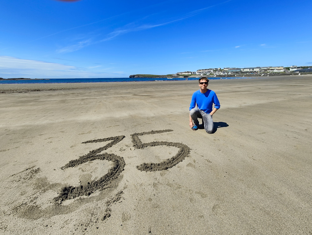 Calum in blue top on Kilkee beach on clear day with 35 written in the sand