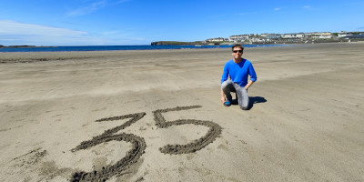 Calum in blue top on Kilkee beach on clear day with 35 written in the sand