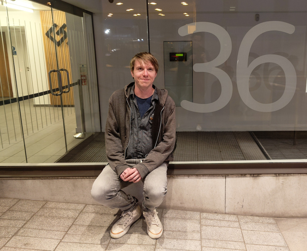 Calum sitting beside an office entrance window with the figure 36 printed on the glass