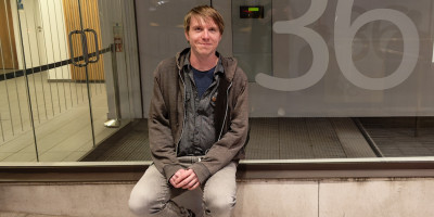 Calum sitting beside an office entrance window with the figure 36 printed on the glass