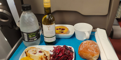 chicken roulade dish, white wine, bread, water bottle and tart on a blue tray
