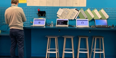 man stands at a blue counter displaying multiple laptops, and accessibility personas described on posters above